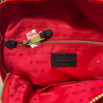 Moschino FW14 McDonald’s Fast Food Backpack is a red nylon backpack from the Autumn/Winter 2014 collection, designed by Jeremy Scott for his debut Moschino lineup. The front features yellow curved arches inspired by McDonald’s branding, with a front zip pocket printed with yellow Moschino text and black “Over 20 Billion Served” slogan. The bag includes gold-tone zippers with black leather pulls, black straps with Moschino logos, a branded interior lining, and comes with a Moschino dust bag. Made in Italy.