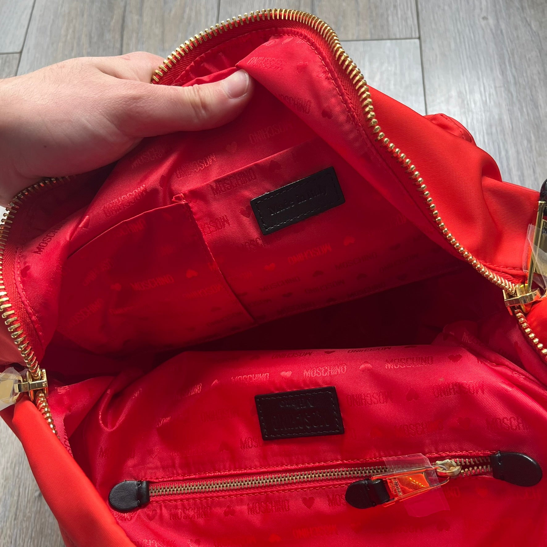 Moschino FW14 McDonald’s Fast Food Backpack is a red nylon backpack from the Autumn/Winter 2014 collection, designed by Jeremy Scott for his debut Moschino lineup. The front features yellow curved arches inspired by McDonald’s branding, with a front zip pocket printed with yellow Moschino text and black “Over 20 Billion Served” slogan. The bag includes gold-tone zippers with black leather pulls, black straps with Moschino logos, a branded interior lining, and comes with a Moschino dust bag. Made in Italy.