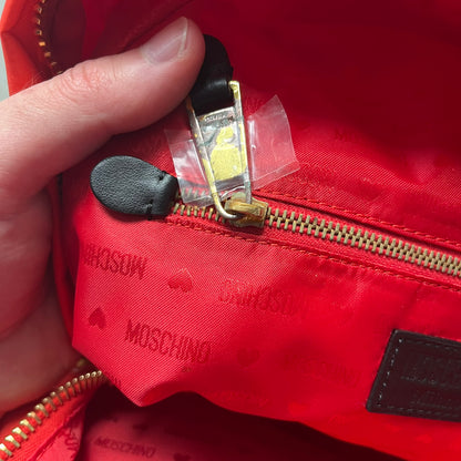 Moschino FW14 McDonald’s Fast Food Backpack is a red nylon backpack from the Autumn/Winter 2014 collection, designed by Jeremy Scott for his debut Moschino lineup. The front features yellow curved arches inspired by McDonald’s branding, with a front zip pocket printed with yellow Moschino text and black “Over 20 Billion Served” slogan. The bag includes gold-tone zippers with black leather pulls, black straps with Moschino logos, a branded interior lining, and comes with a Moschino dust bag. Made in Italy.