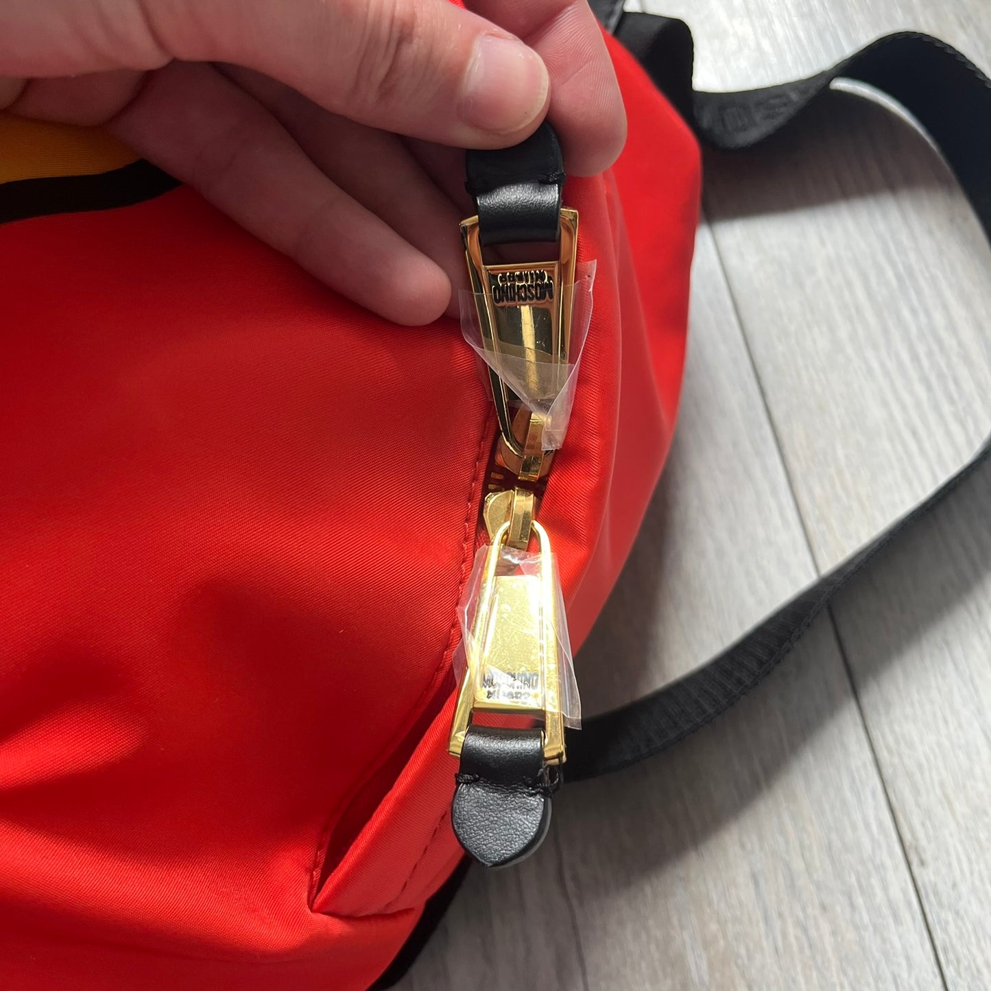 Moschino FW14 McDonald’s Fast Food Backpack is a red nylon backpack from the Autumn/Winter 2014 collection, designed by Jeremy Scott for his debut Moschino lineup. The front features yellow curved arches inspired by McDonald’s branding, with a front zip pocket printed with yellow Moschino text and black “Over 20 Billion Served” slogan. The bag includes gold-tone zippers with black leather pulls, black straps with Moschino logos, a branded interior lining, and comes with a Moschino dust bag. Made in Italy.