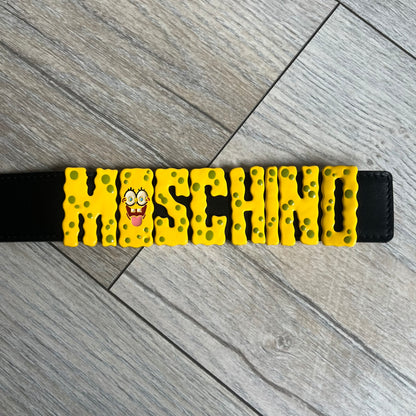 Moschino FW14 SpongeBob Leather Belt is a black leather belt from the Fall/Winter 2014 SpongeBob SquarePants collaboration. The front features the MOSCHINO logo formed by individual movable letters rather than a single rigid buckle. Each letter is finished in yellow with green sponge-like detailing, and the first “O” includes SpongeBob’s happy face. The belt uses a metal buckle closure and comes with the original dust bag and tags. Made in Italy from Genuine Leather.