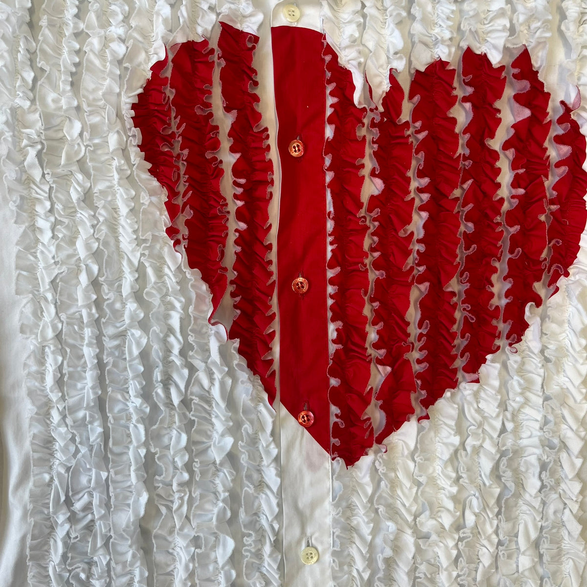 Moschino SS2000 Ruffled Heart Button Up Shirt is a white button-up made in Italy, featuring a ruffled rectangular panel on the front with an asymmetrically placed red heart at its center. It has Moschino-branded buttons, and a black Moschino text logo sits on the back just below the collar.