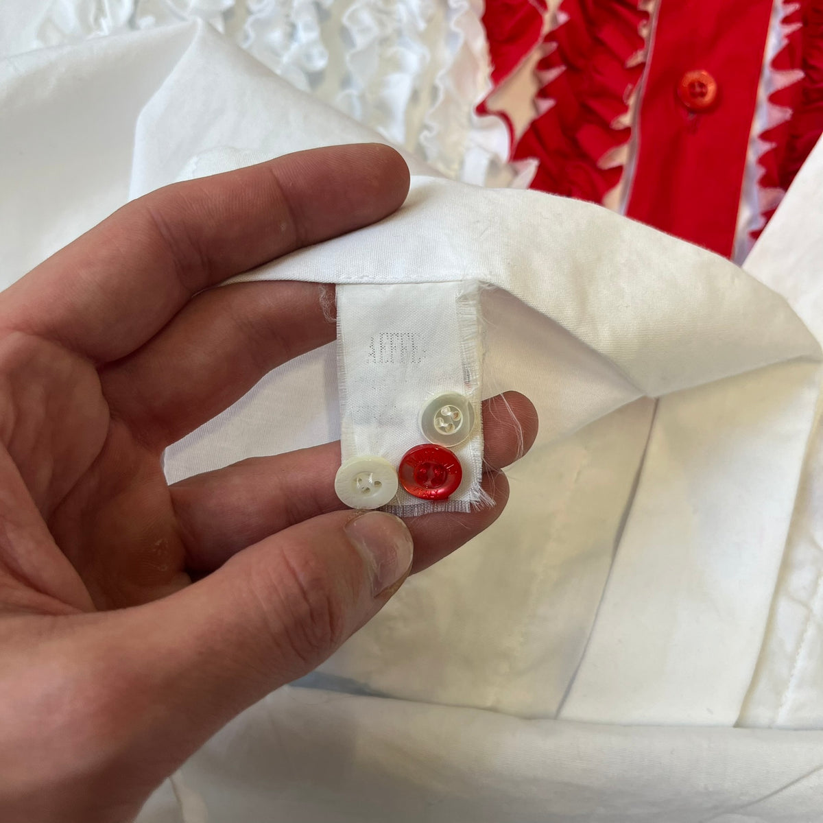 Moschino SS2000 Ruffled Heart Button Up Shirt is a white button-up made in Italy, featuring a ruffled rectangular panel on the front with an asymmetrically placed red heart at its center. It has Moschino-branded buttons, and a black Moschino text logo sits on the back just below the collar.