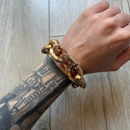 Moschino x H&M 2018 Gold Bracelet is a chunky chain bracelet released as part of the Moschino x H&M collaboration designed by Jeremy Scott. The bracelet features oversized O-shaped links in a gold-tone finish and a T-bar clasp closure. Produced for the 2018 capsule collection and made in Vietnam, it comes with the original white H&MOSCHINO box.