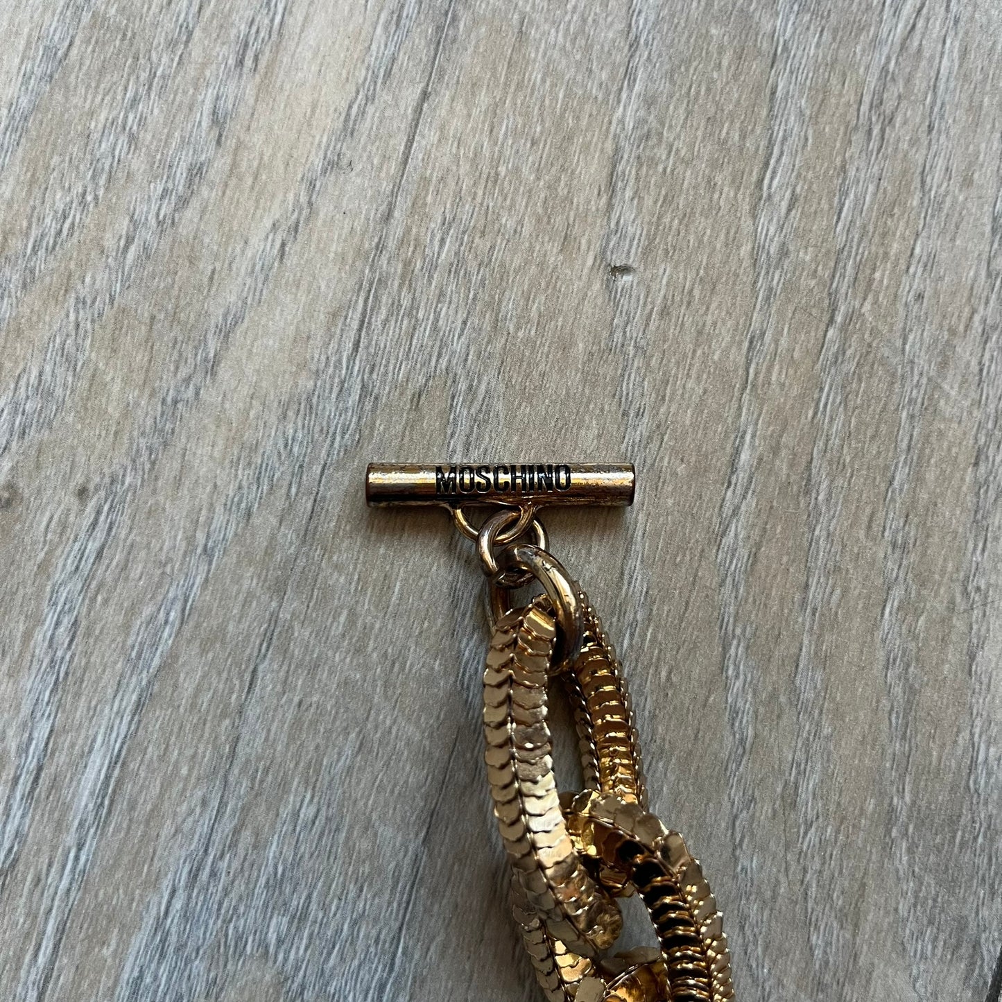 Moschino x H&M 2018 Gold Bracelet is a chunky chain bracelet released as part of the Moschino x H&M collaboration designed by Jeremy Scott. The bracelet features oversized O-shaped links in a gold-tone finish and a T-bar clasp closure. Produced for the 2018 capsule collection and made in Vietnam, it comes with the original white H&MOSCHINO box.