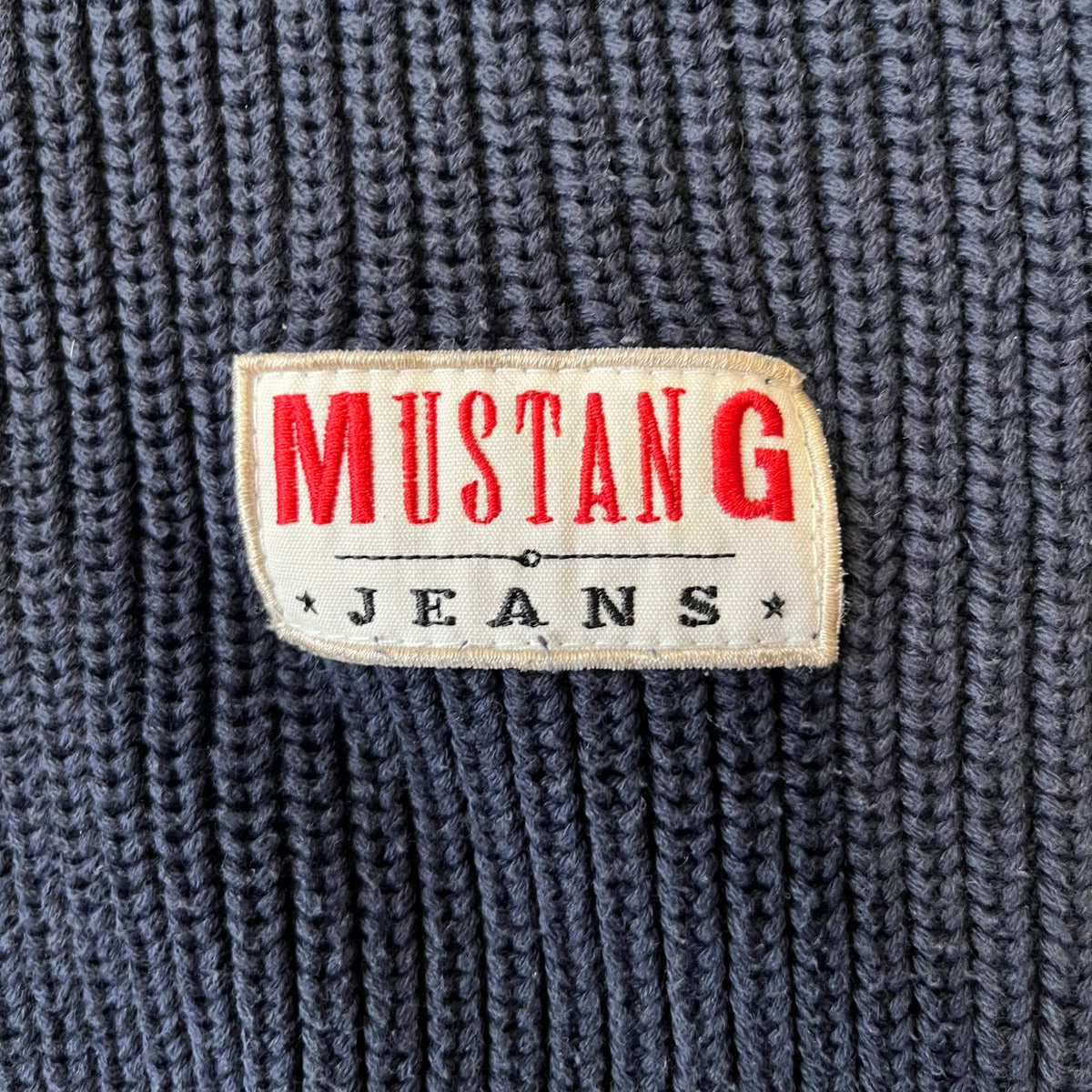 Mustang Jeans Navy Troyer Sweater is a heavyweight, high-quality navy troyer sweater featuring a Mustang Jeans patch tag on the lower front and a silver-colored horse zipper pull. The design includes a collar typical of the troyer style.