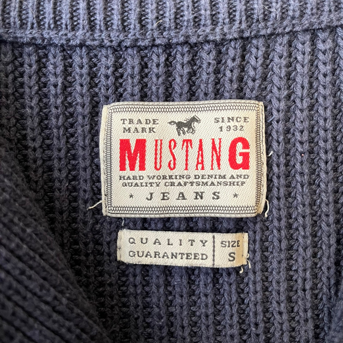 Mustang Jeans Navy Troyer Sweater is a heavyweight, high-quality navy troyer sweater featuring a Mustang Jeans patch tag on the lower front and a silver-colored horse zipper pull. The design includes a collar typical of the troyer style.