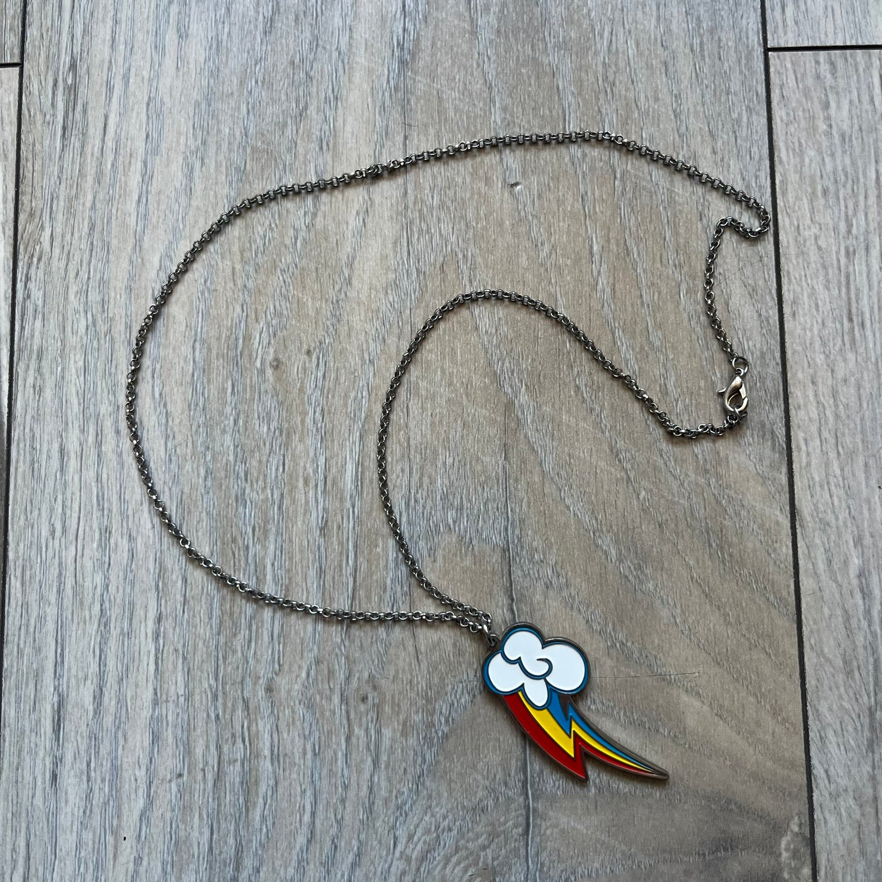 My Little Pony Rainbow Dash 2010s Necklace produced by WeLoveFine. Constructed from stainless steel, it features a slightly raised steel outline pendant of the Rainbow Dash cloud and three-color lightning bolt logo, finished with enamel detailing. The pendant is attached to a thin stainless steel chain.