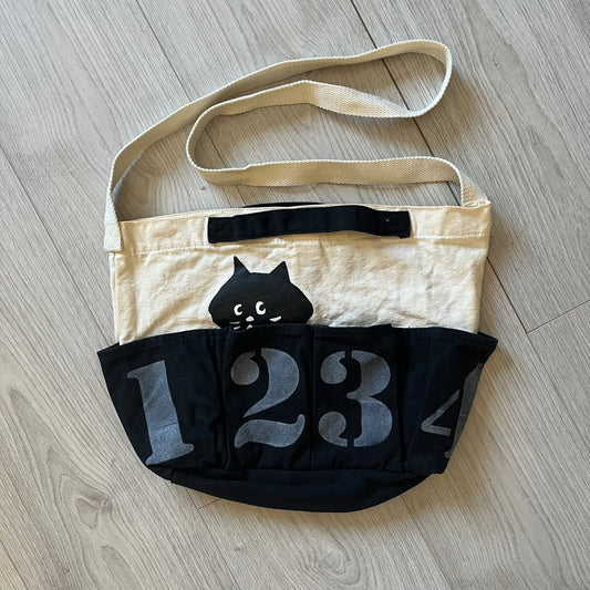 Beige bag with black cat design and number '123' on a wooden floor