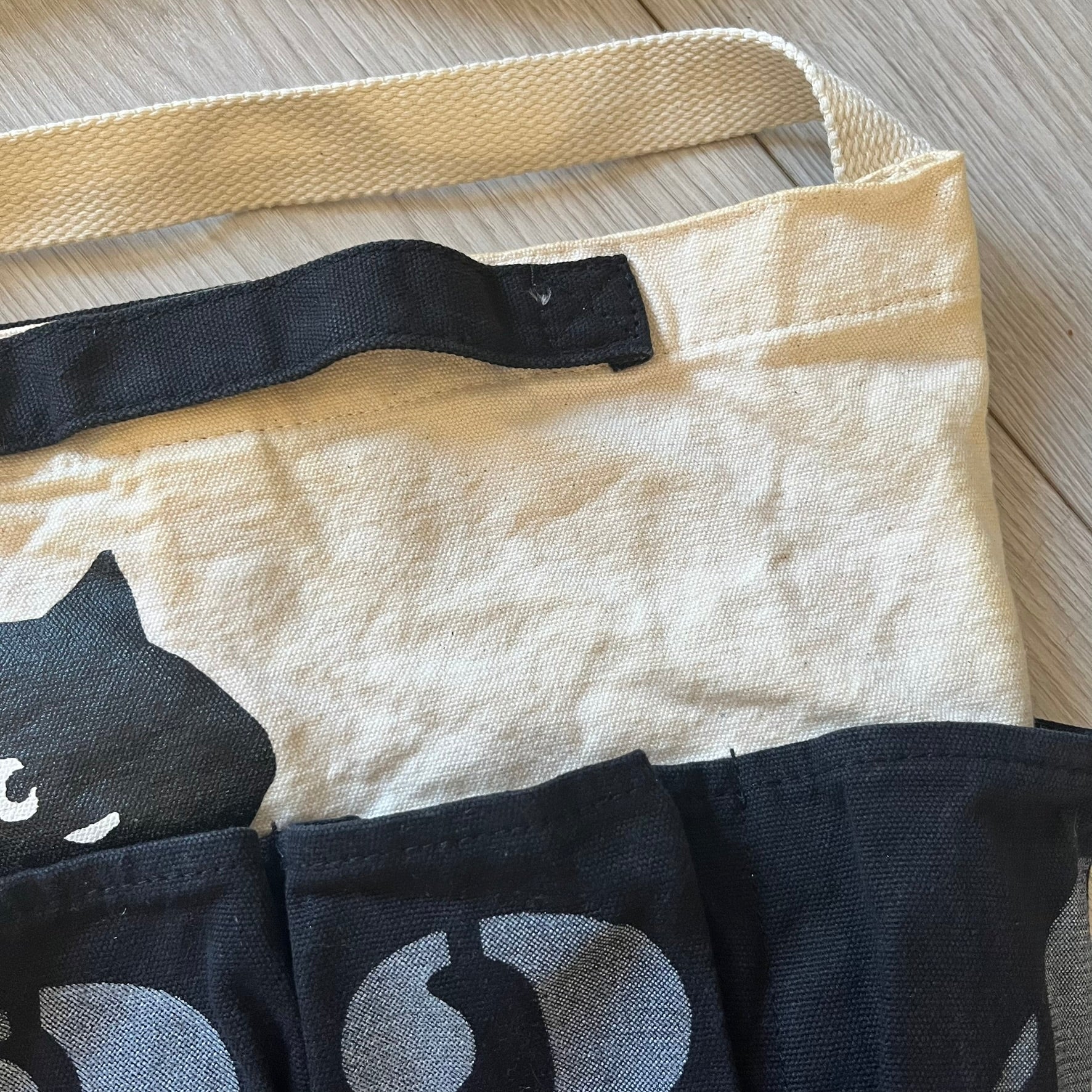 Beige tote bag with black cat design on a wooden surface
