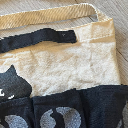 Beige tote bag with black cat design on a wooden surface