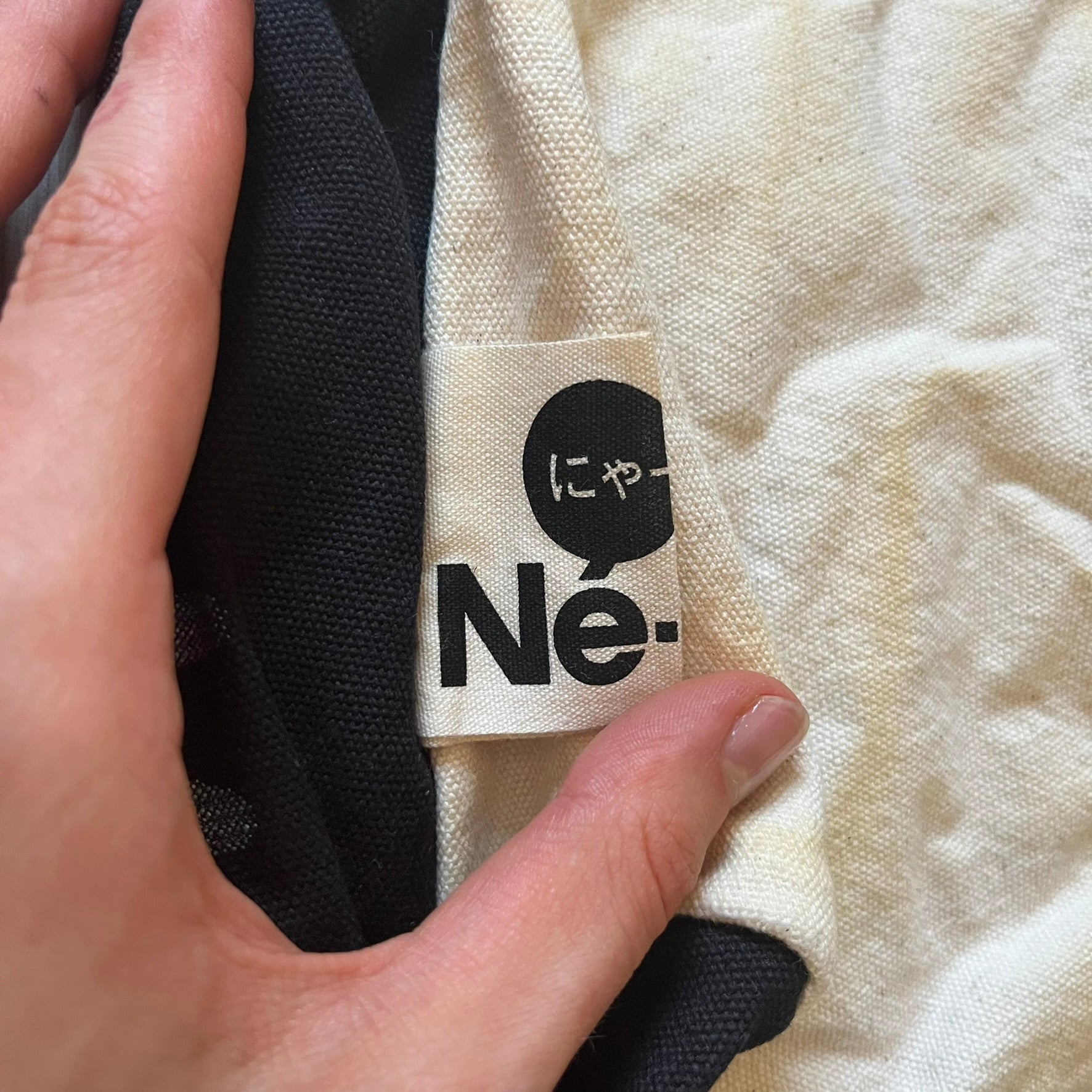 Close-up of a label on a garment with text and a logo, held by a hand.
