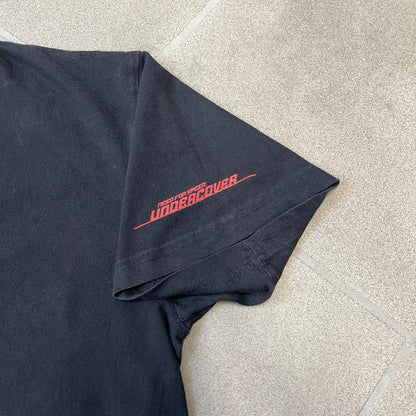 Need for Speed Undercover 2008 Promo Tee is a washed black T-shirt made on a Stedman blank, featuring a full red graphic along the bottom of a woman, palm trees, and a car with the Need for Speed Undercover logo. A red NFS logo is also printed on one sleeve.