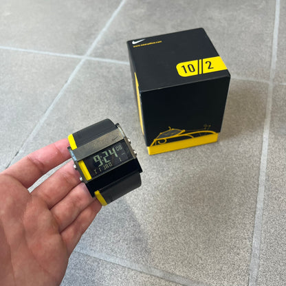 Nike 10//2 Lance Armstrong 2005 Signature Digital Watch features a black stainless steel case with a black LCD display and a black waterproof leather strap with a bright yellow accent. It has a 100-hour chronograph, interval timer, three time alarms, hydration alarm, and data recall, with water resistance to 100 meters. The strap has engraved date and time markings, and the watch comes with the original box and papers.
