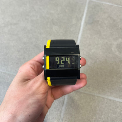 Nike 10//2 Lance Armstrong 2005 Signature Digital Watch features a black stainless steel case with a black LCD display and a black waterproof leather strap with a bright yellow accent. It has a 100-hour chronograph, interval timer, three time alarms, hydration alarm, and data recall, with water resistance to 100 meters. The strap has engraved date and time markings, and the watch comes with the original box and papers.
