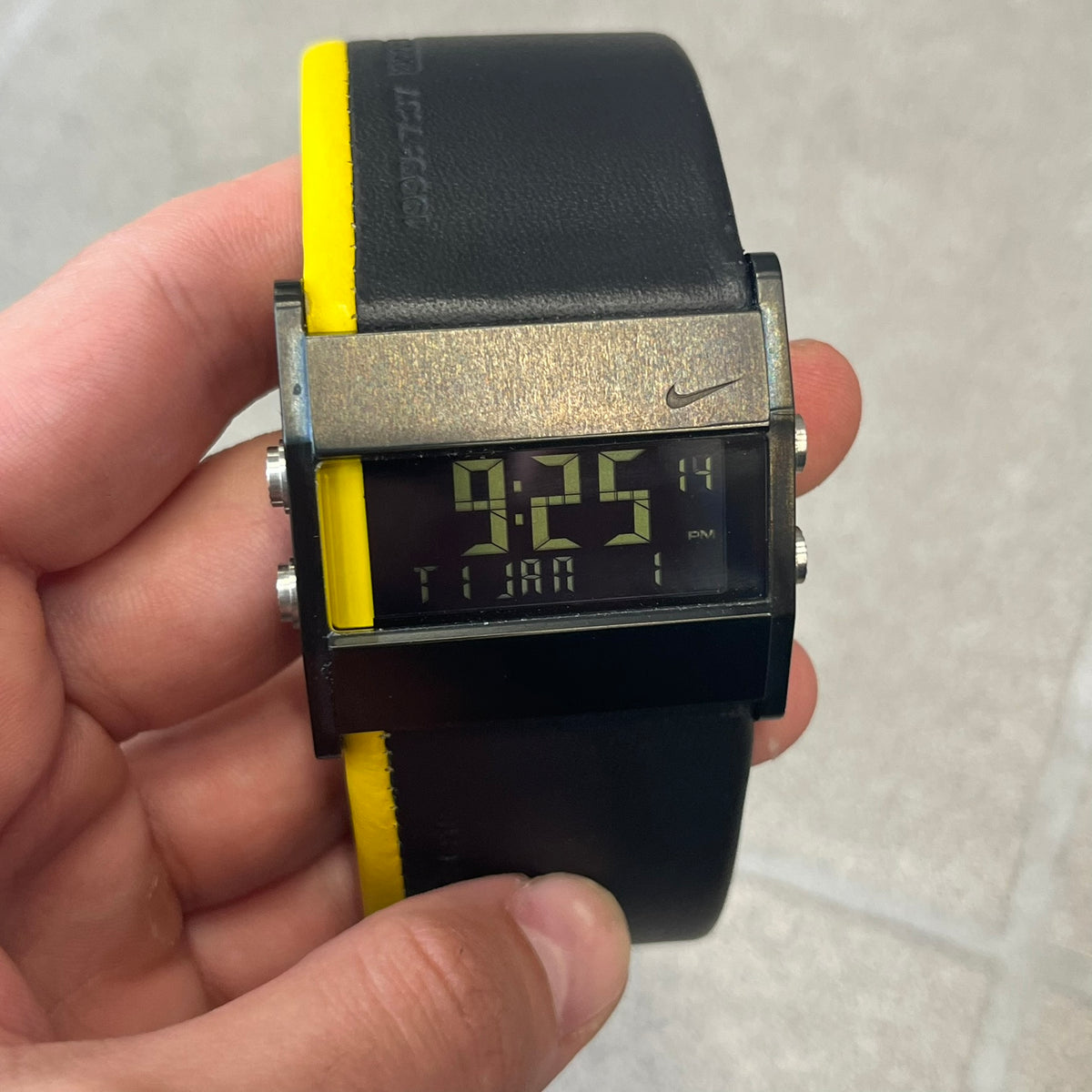 Nike 10//2 Lance Armstrong 2005 Signature Digital Watch features a black stainless steel case with a black LCD display and a black waterproof leather strap with a bright yellow accent. It has a 100-hour chronograph, interval timer, three time alarms, hydration alarm, and data recall, with water resistance to 100 meters. The strap has engraved date and time markings, and the watch comes with the original box and papers.
