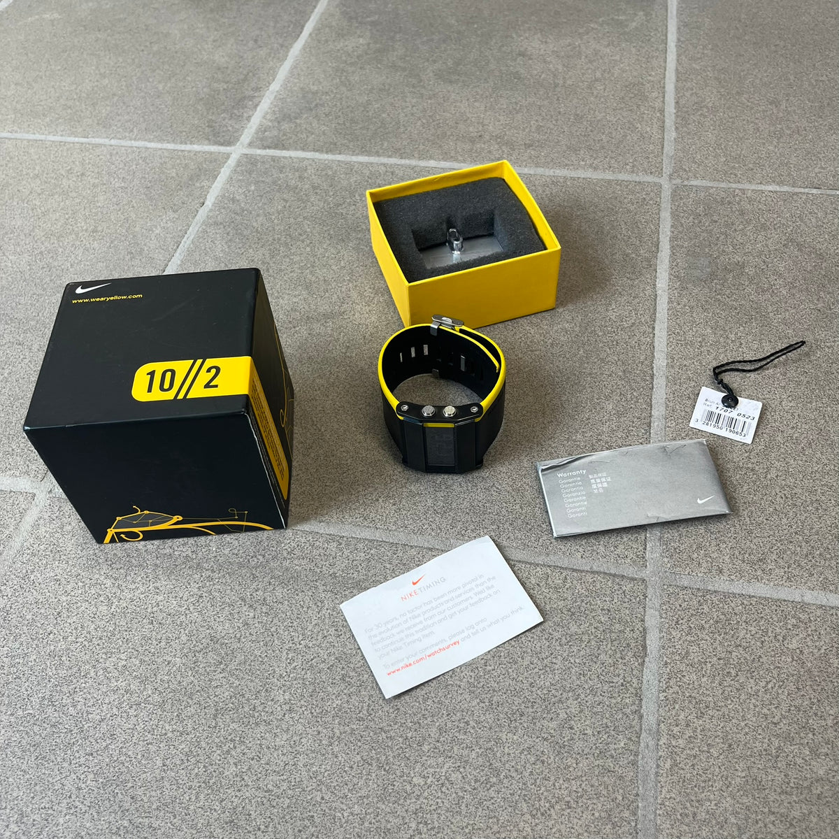 Nike 10//2 Lance Armstrong 2005 Signature Digital Watch features a black stainless steel case with a black LCD display and a black waterproof leather strap with a bright yellow accent. It has a 100-hour chronograph, interval timer, three time alarms, hydration alarm, and data recall, with water resistance to 100 meters. The strap has engraved date and time markings, and the watch comes with the original box and papers.

