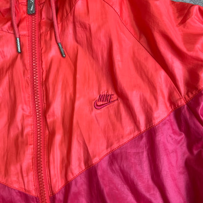 Nike 2000s Black Stars Red Windbreaker features a two-tone red design with a lighter red upper section and a darker red lower half. It is detailed with black star patches running along one sleeve and an additional star patch on the front. The jacket includes two zip pockets.