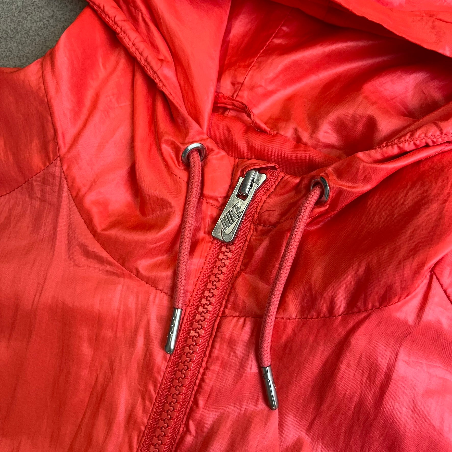 Nike 2000s Black Stars Red Windbreaker features a two-tone red design with a lighter red upper section and a darker red lower half. It is detailed with black star patches running along one sleeve and an additional star patch on the front. The jacket includes two zip pockets.