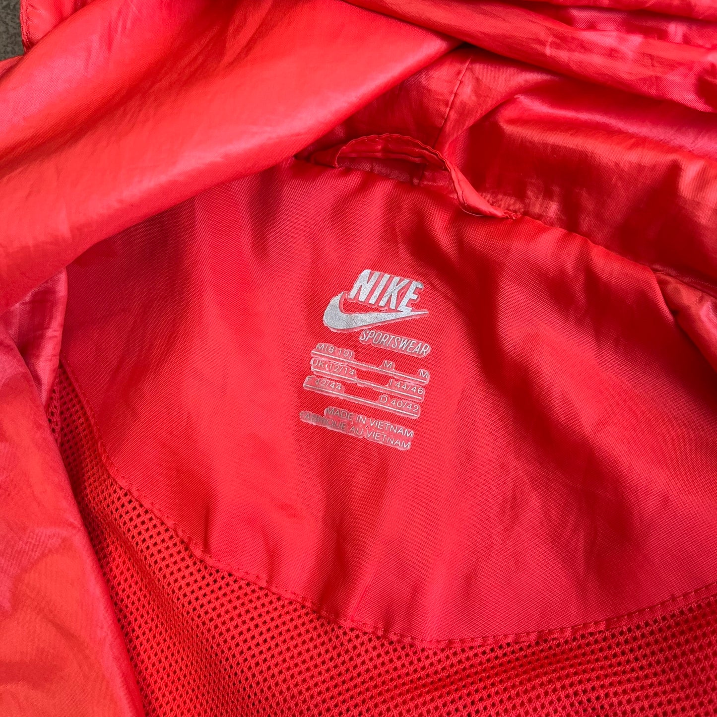 Nike 2000s Black Stars Red Windbreaker features a two-tone red design with a lighter red upper section and a darker red lower half. It is detailed with black star patches running along one sleeve and an additional star patch on the front. The jacket includes two zip pockets.