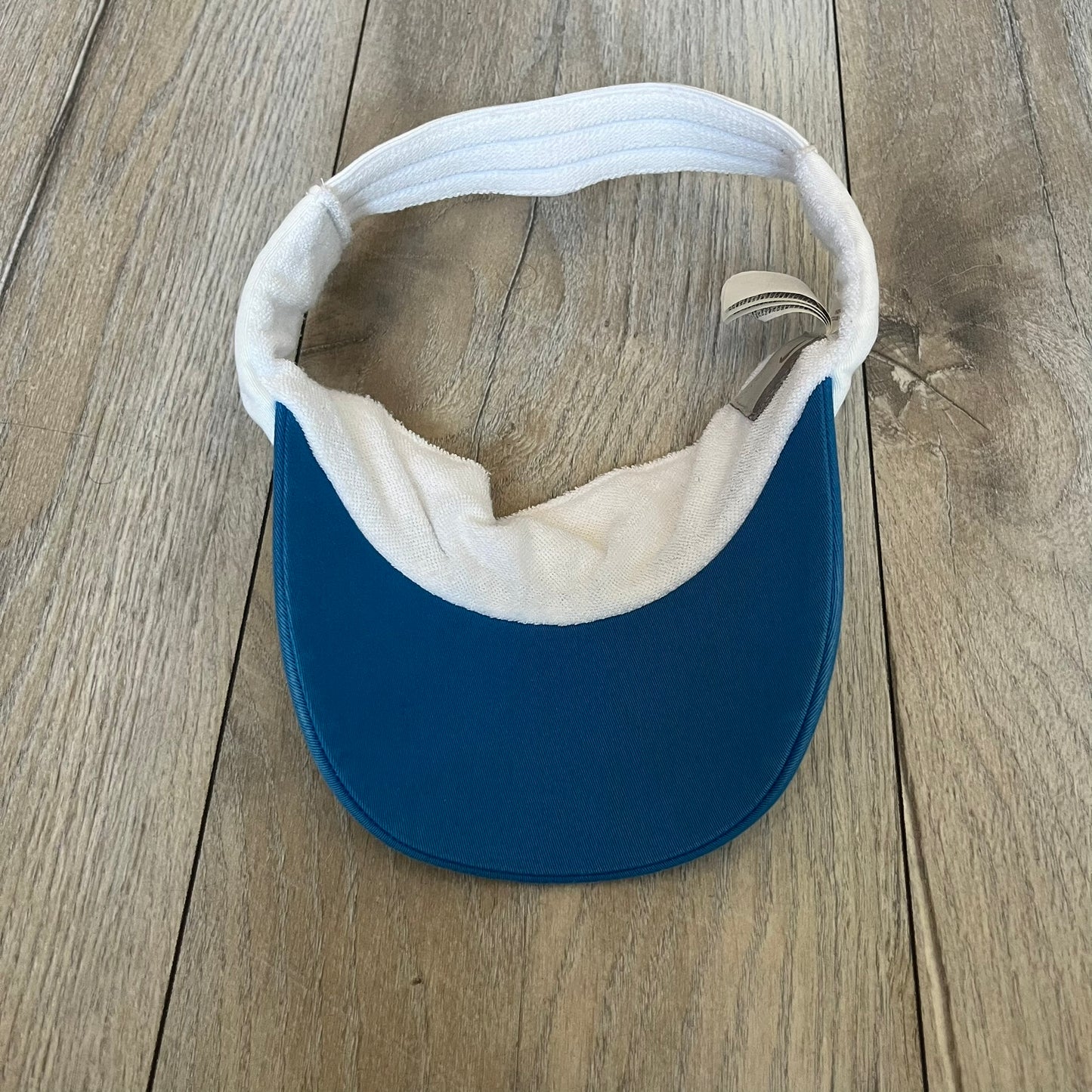 Nike 2000s Blue & White Tennis Visor is a youth-size visor cap featuring a white crown with blue trim running along the edge. The front includes a navy and white Nike logo, while the underside of the brim is finished in blue. The visor is designed with a soft, comfortable headband-style strap for a secure fit.
