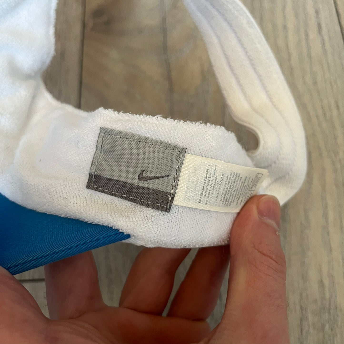 Nike 2000s Blue & White Tennis Visor is a youth-size visor cap featuring a white crown with blue trim running along the edge. The front includes a navy and white Nike logo, while the underside of the brim is finished in blue. The visor is designed with a soft, comfortable headband-style strap for a secure fit.