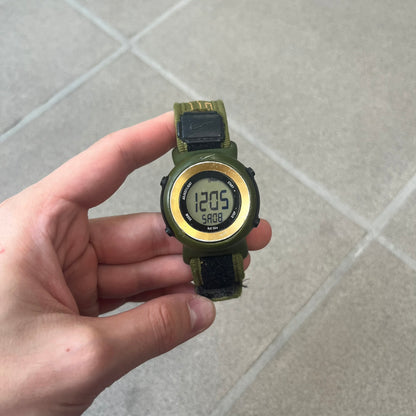 Nike 2000's Gorge Sport WK0013 Digital Watch is a vintage digital watch featuring a green circular face framed by a gold ring, water resistant up to 50m. It's fitted with a green canvas strap accented with orange line patterns and a black leather tab bearing the Nike logo.