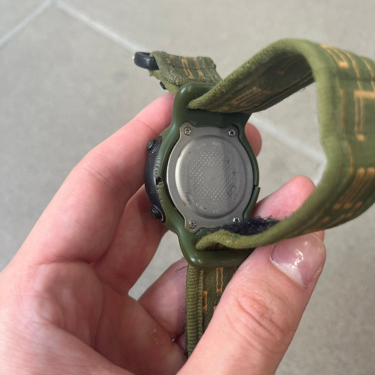 Nike 2000's Gorge Sport WK0013 Digital Watch is a vintage digital watch featuring a green circular face framed by a gold ring, water resistant up to 50m. It's fitted with a green canvas strap accented with orange line patterns and a black leather tab bearing the Nike logo.