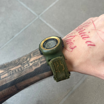 Nike 2000's Gorge Sport WK0013 Digital Watch is a vintage digital watch featuring a green circular face framed by a gold ring, water resistant up to 50m. It's fitted with a green canvas strap accented with orange line patterns and a black leather tab bearing the Nike logo.