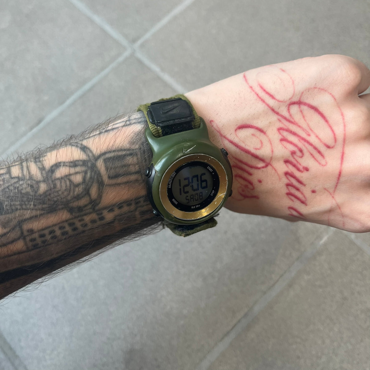 Nike 2000's Gorge Sport WK0013 Digital Watch is a vintage digital watch featuring a green circular face framed by a gold ring, water resistant up to 50m. It's fitted with a green canvas strap accented with orange line patterns and a black leather tab bearing the Nike logo.