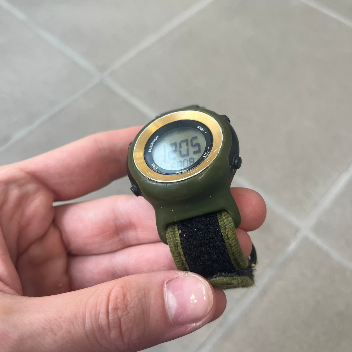 Nike 2000's Gorge Sport WK0013 Digital Watch is a vintage digital watch featuring a green circular face framed by a gold ring, water resistant up to 50m. It's fitted with a green canvas strap accented with orange line patterns and a black leather tab bearing the Nike logo.