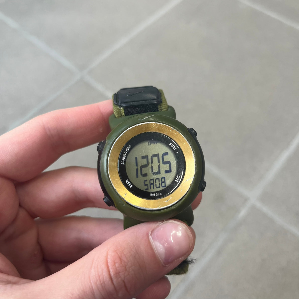 Nike 2000's Gorge Sport WK0013 Digital Watch is a vintage digital watch featuring a green circular face framed by a gold ring, water resistant up to 50m. It's fitted with a green canvas strap accented with orange line patterns and a black leather tab bearing the Nike logo.