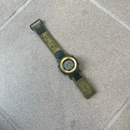 Nike 2000's Gorge Sport WK0013 Digital Watch is a vintage digital watch featuring a green circular face framed by a gold ring, water resistant up to 50m. It's fitted with a green canvas strap accented with orange line patterns and a black leather tab bearing the Nike logo.