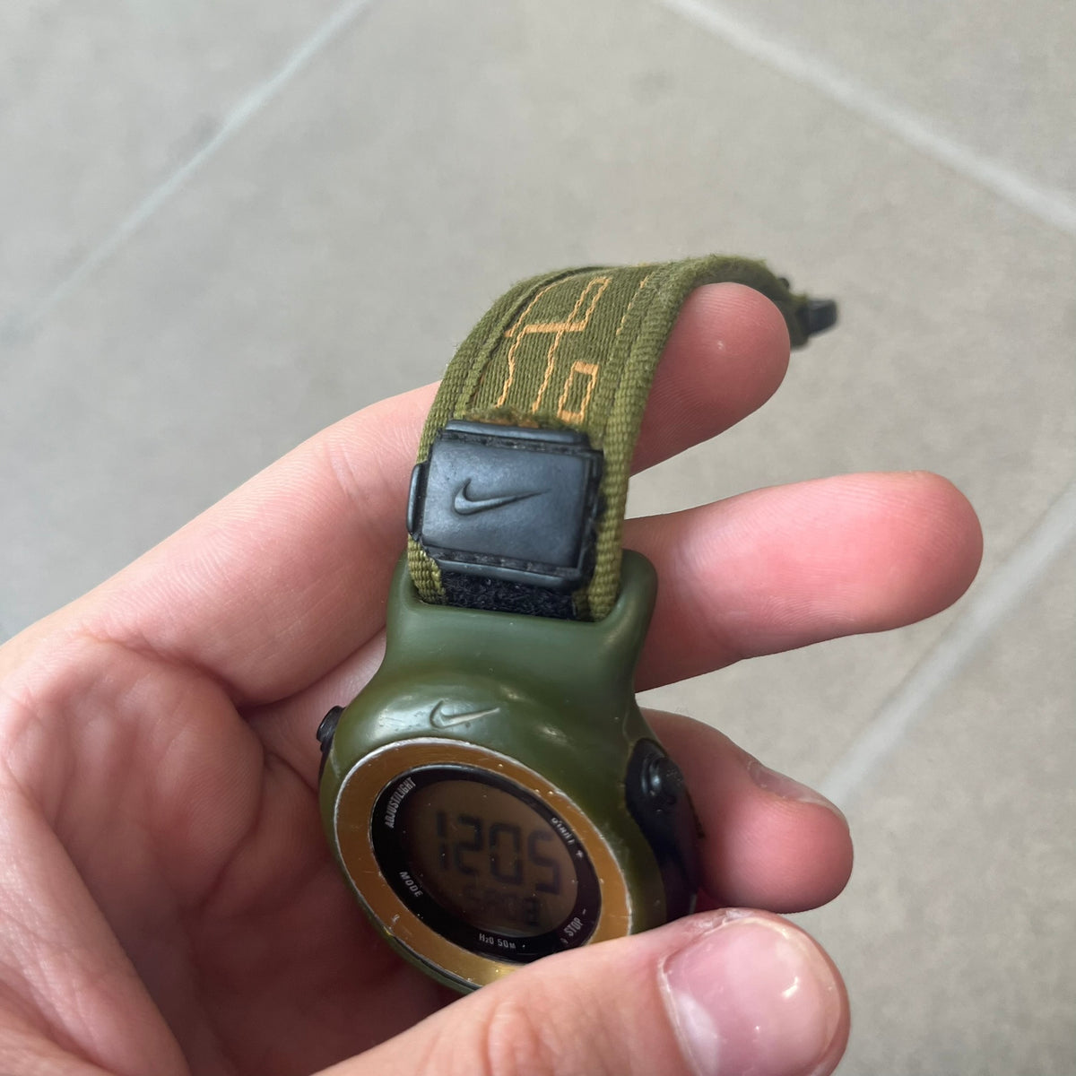 Nike 2000's Gorge Sport WK0013 Digital Watch is a vintage digital watch featuring a green circular face framed by a gold ring, water resistant up to 50m. It's fitted with a green canvas strap accented with orange line patterns and a black leather tab bearing the Nike logo.