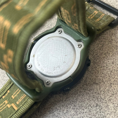 Nike 2000's Gorge Sport WK0013 Digital Watch is a vintage digital watch featuring a green circular face framed by a gold ring, water resistant up to 50m. It's fitted with a green canvas strap accented with orange line patterns and a black leather tab bearing the Nike logo.