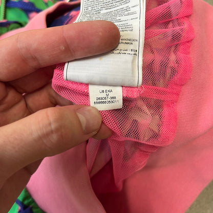 Nike 2000's Green & Pink Camo Windbreaker features an all-over camouflage pattern with a green base and pink and purple details. It has pink hems, a pink mesh lining, and a gold-tone 3D Nike shoe zipper pull, while the pocket zippers feature Nike Air logos. The chest has a gold-tone metal Nike Air logo.
