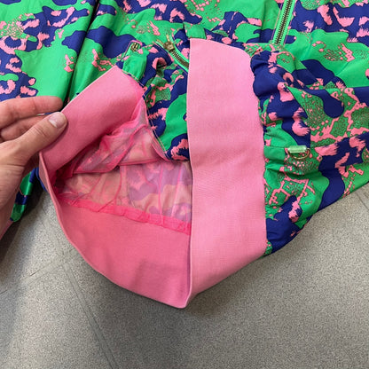 Nike 2000's Green & Pink Camo Windbreaker features an all-over camouflage pattern with a green base and pink and purple details. It has pink hems, a pink mesh lining, and a gold-tone 3D Nike shoe zipper pull, while the pocket zippers feature Nike Air logos. The chest has a gold-tone metal Nike Air logo.

