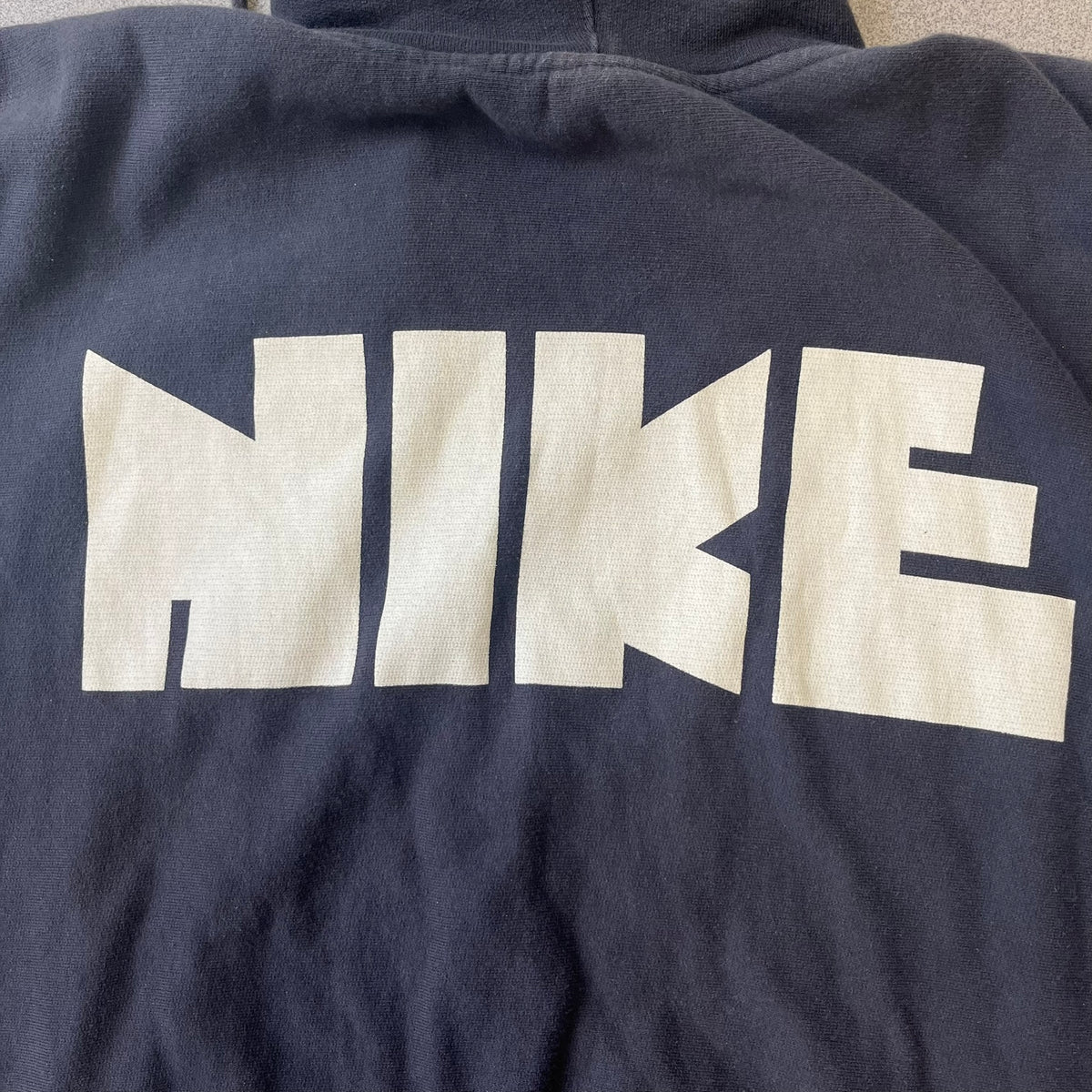 Nike 2010’s Big Logo Black Hoodie is a limited-edition black washed zip hoodie made in Portugal, with a white Nike logo on the chest and a larger one across the upper back, both non-standard designs. It has a standard zipper and a neck tag styled after Nike’s 1980s tags, and the whole piece is finished to look vintage.