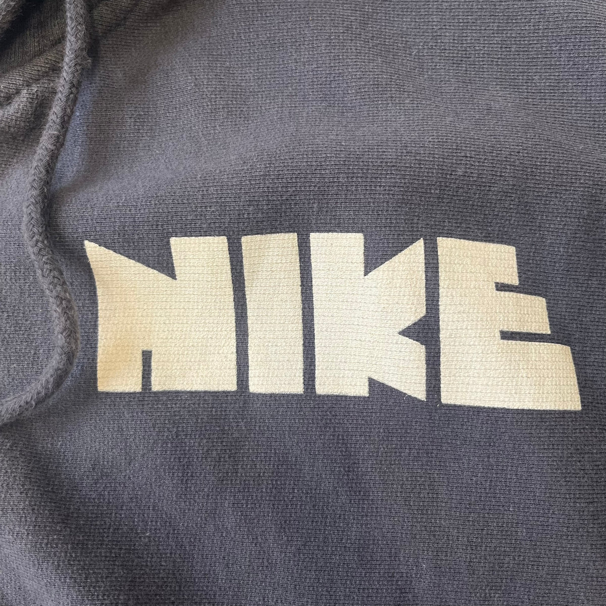 Nike 2010’s Big Logo Black Hoodie is a limited-edition black washed zip hoodie made in Portugal, with a white Nike logo on the chest and a larger one across the upper back, both non-standard designs. It has a standard zipper and a neck tag styled after Nike’s 1980s tags, and the whole piece is finished to look vintage.