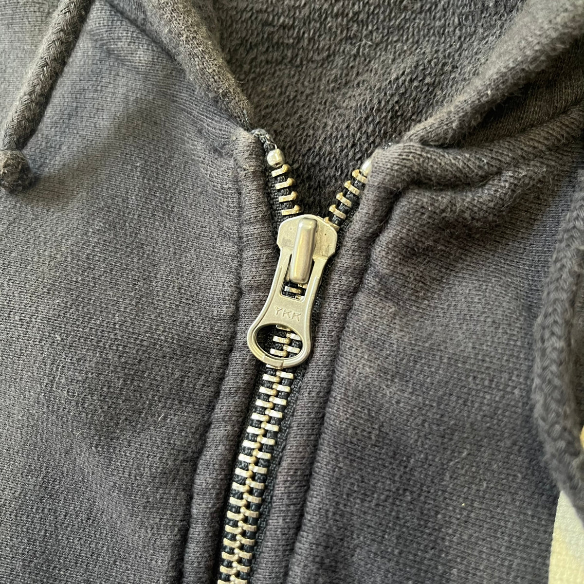 Nike 2010’s Big Logo Black Hoodie is a limited-edition black washed zip hoodie made in Portugal, with a white Nike logo on the chest and a larger one across the upper back, both non-standard designs. It has a standard zipper and a neck tag styled after Nike’s 1980s tags, and the whole piece is finished to look vintage.