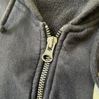 Nike 2010’s Big Logo Black Hoodie is a limited-edition black washed zip hoodie made in Portugal, with a white Nike logo on the chest and a larger one across the upper back, both non-standard designs. It has a standard zipper and a neck tag styled after Nike’s 1980s tags, and the whole piece is finished to look vintage.