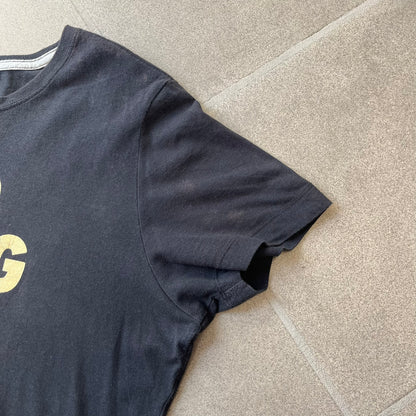 Nike 2012 Olympics “Gold Digging” Black Tee features a black slim-fit T-shirt with gold “Gold Digging” text on the front and a small Nike logo underneath. The design was released in connection with the 2012 Olympics and was later discontinued following controversy surrounding the wording.
