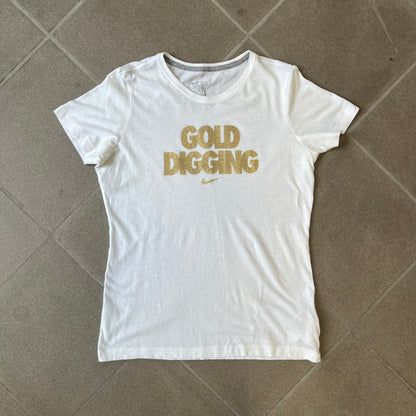 Nike 2012 Olympics “Gold Digging” White Tee features a white slim-fit T-shirt with gold “Gold Digging” text on the front and a small Nike logo underneath. The design was released in connection with the 2012 Olympics and was later discontinued following controversy surrounding the wording.