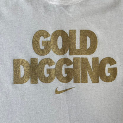 Nike 2012 Olympics “Gold Digging” White Tee features a white slim-fit T-shirt with gold “Gold Digging” text on the front and a small Nike logo underneath. The design was released in connection with the 2012 Olympics and was later discontinued following controversy surrounding the wording.