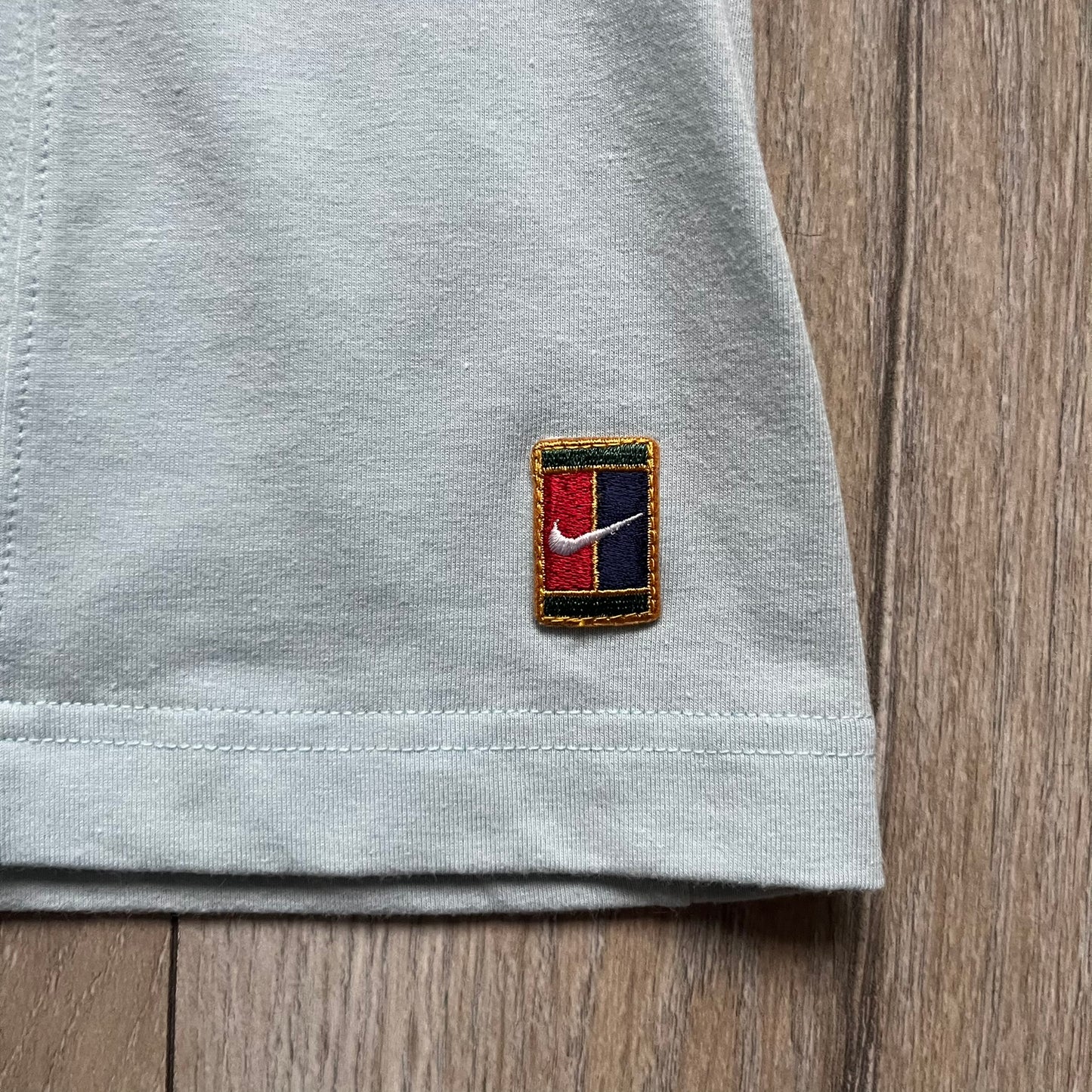 Nike 90’s Challenge Court Tennis Skirt is a baby blue women’s tennis skirt made in Thailand. It features a small green and red Nike Court logo patch at the lower hem, a Dri-FIT patch at the top, and an adjustable waistband with drawstrings.&nbsp;