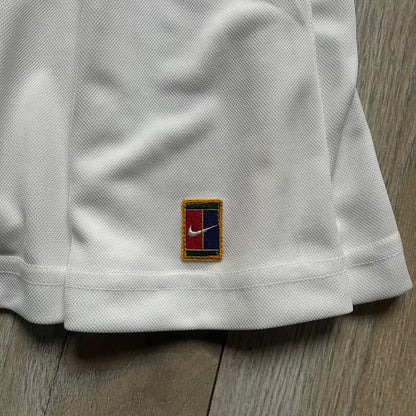 Nike 90’s Challenge Court Tennis Skirt is a white women’s tennis skirt made in USA. It features a small green and red Nike Court logo patch at the lower hem, a Dri-FIT patch at the top, and an adjustable waistband with drawstrings.