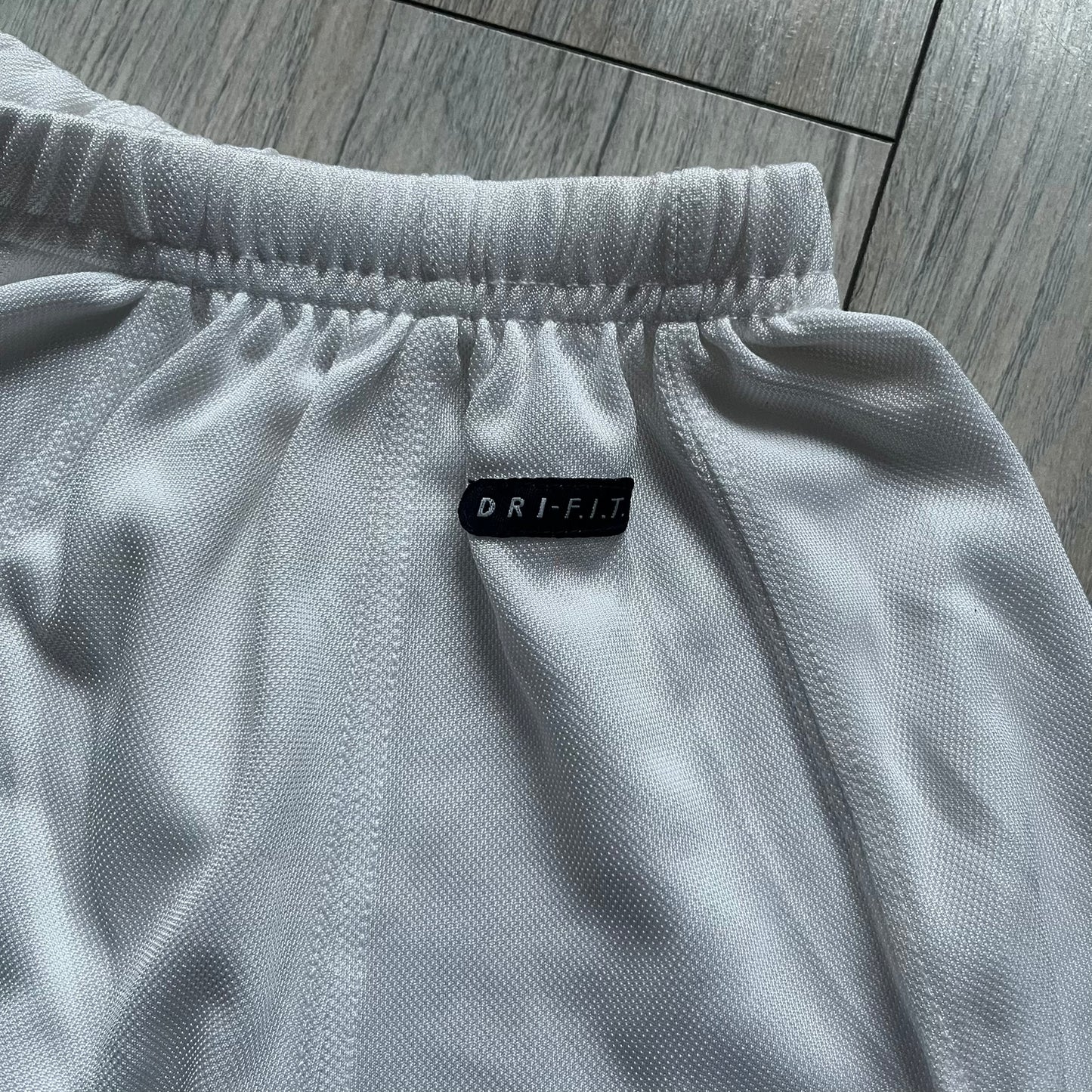 Nike 90’s Challenge Court Tennis Skirt is a white women’s tennis skirt made in USA. It features a small green and red Nike Court logo patch at the lower hem, a Dri-FIT patch at the top, and an adjustable waistband with drawstrings.