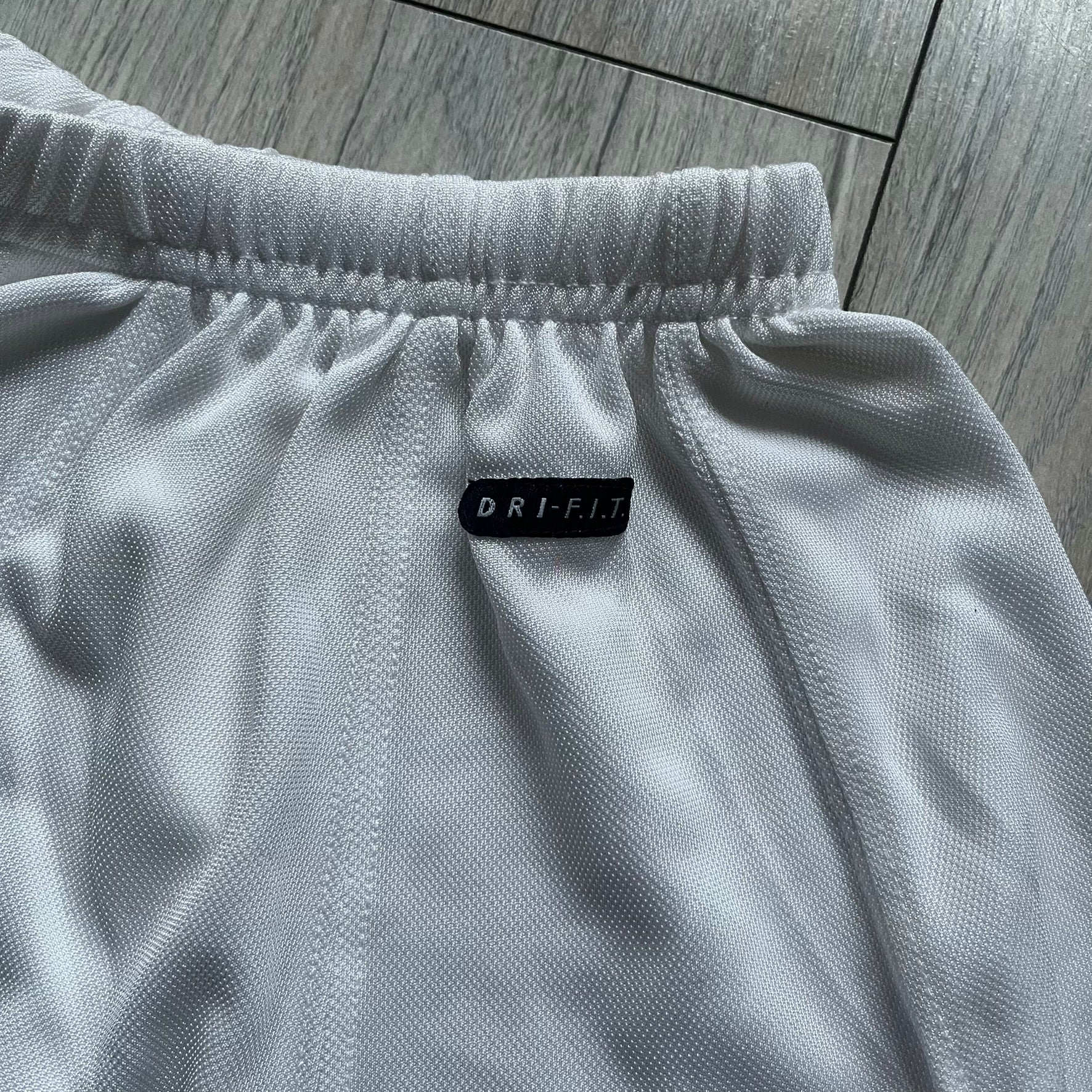 Nike 90’s Challenge Court Tennis Skirt is a white women’s tennis skirt made in USA. It features a small green and red Nike Court logo patch at the lower hem, a Dri-FIT patch at the top, and an adjustable waistband with drawstrings.