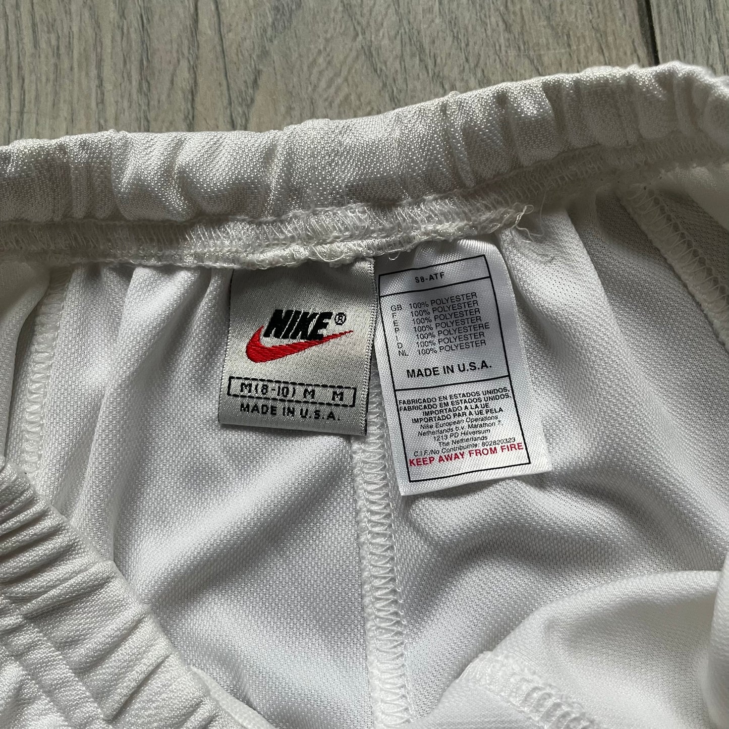 Nike 90’s Challenge Court Tennis Skirt is a white women’s tennis skirt made in USA. It features a small green and red Nike Court logo patch at the lower hem, a Dri-FIT patch at the top, and an adjustable waistband with drawstrings.