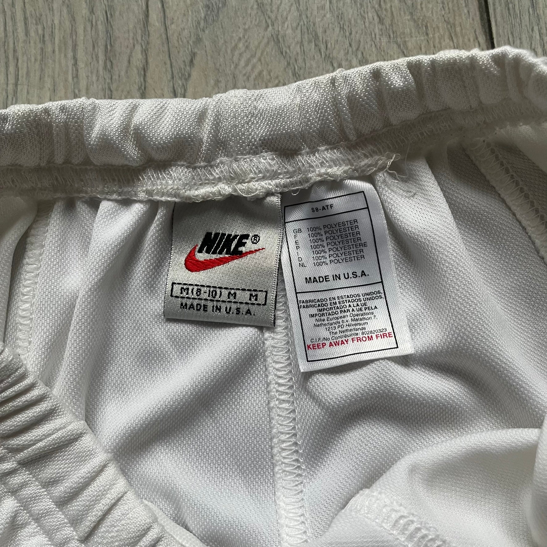 Nike 90’s Challenge Court Tennis Skirt is a white women’s tennis skirt made in USA. It features a small green and red Nike Court logo patch at the lower hem, a Dri-FIT patch at the top, and an adjustable waistband with drawstrings.